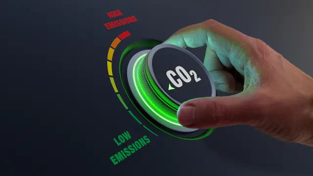 Hand dreht einen Regler von hohen zu niedrigen CO₂-Emissionen